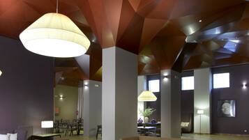 Een moderne lobby met een geometrisch plafondontwerp, een centrale salontafel, banken en een eethoek op de achtergrond.