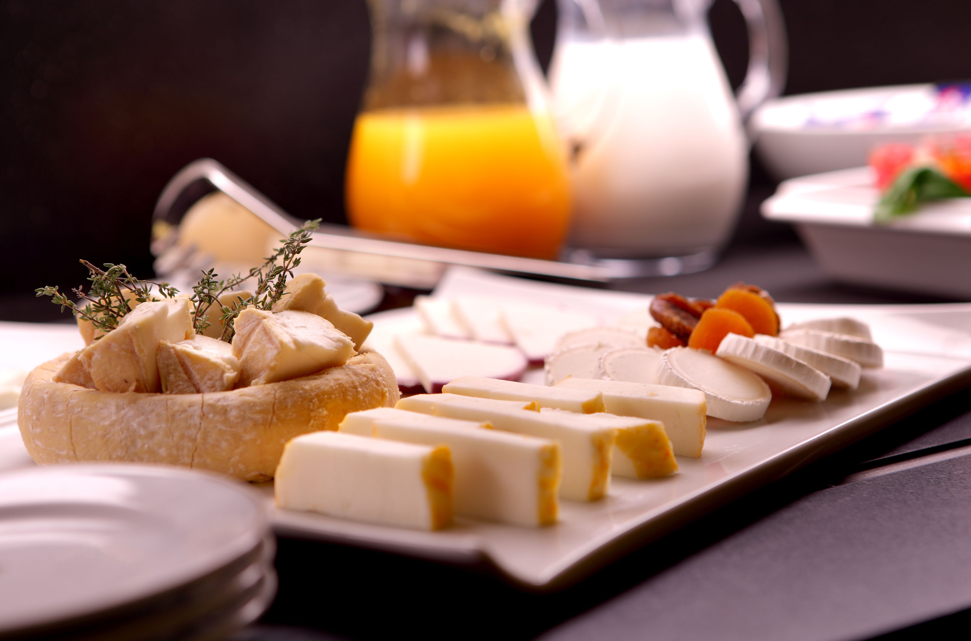 A breakfast setting with various cheeses, fruits, and a jug of orange juice.