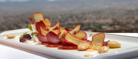 A white rectangular plate with a food arrangement featuring apple slices and nuts, set against a blurred mountain backdrop.