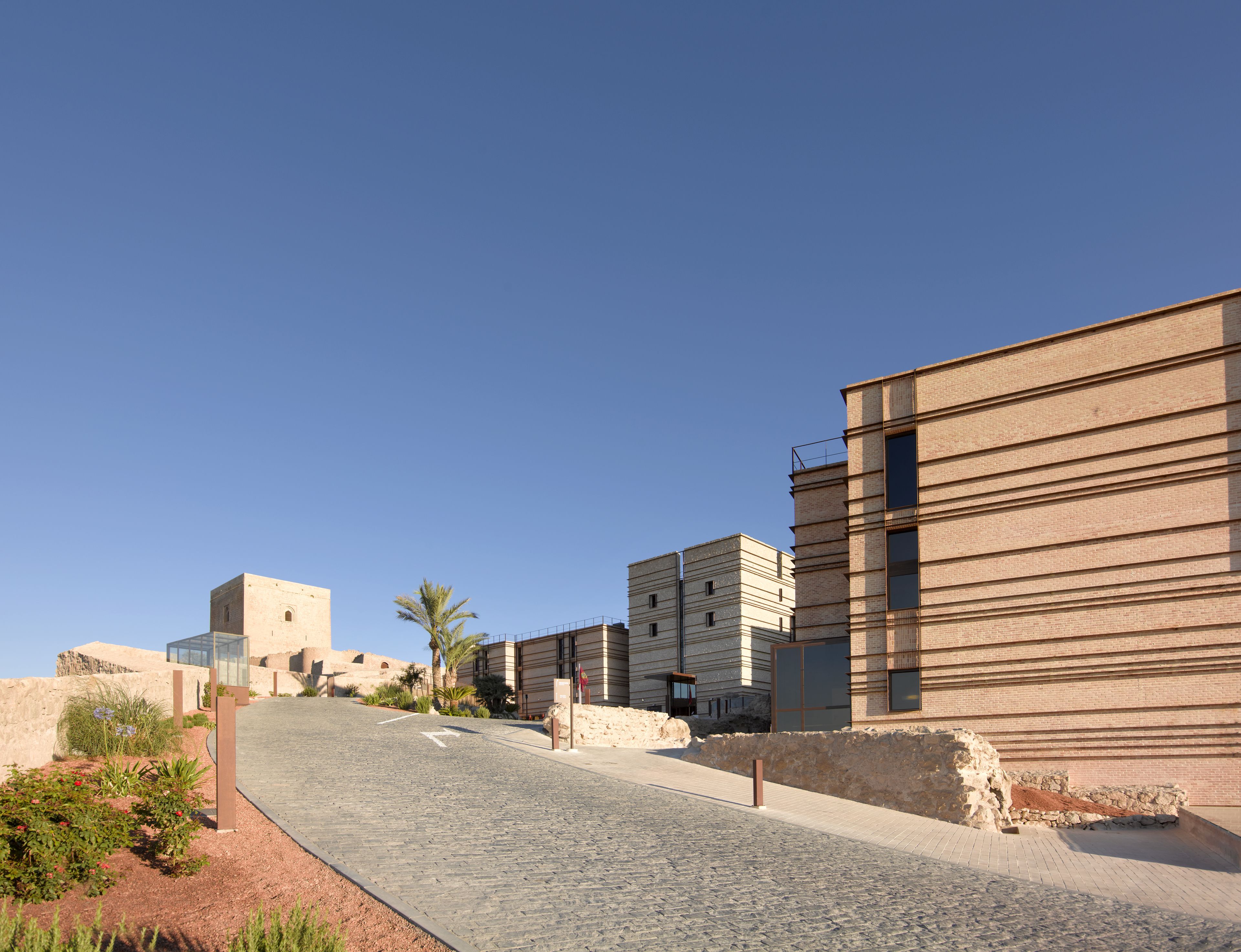 A modern urban street with buildings, a cobblestone road, and a clear blue sky.