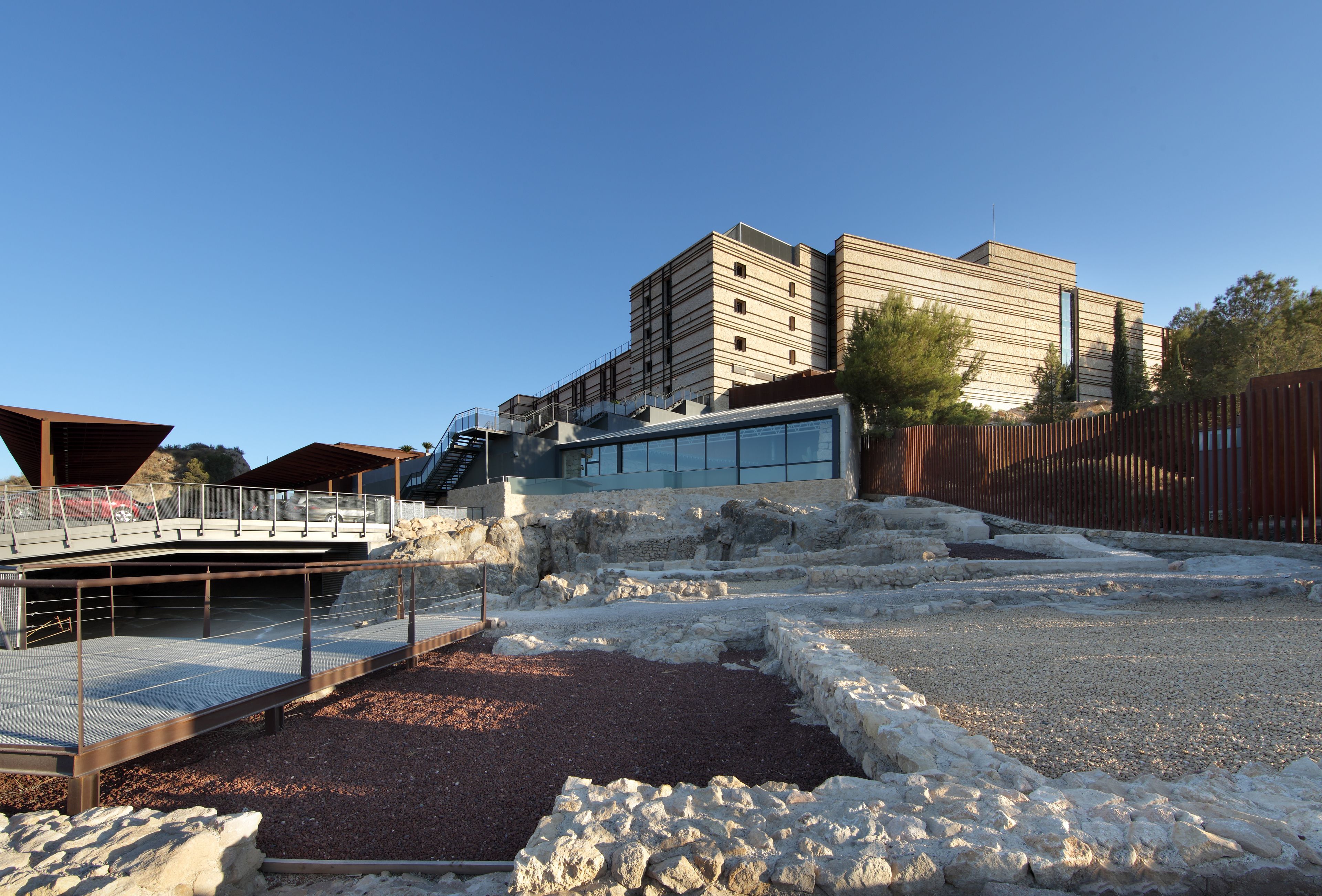 A modern building with a glass facade and a stone pathway leading to a covered area.