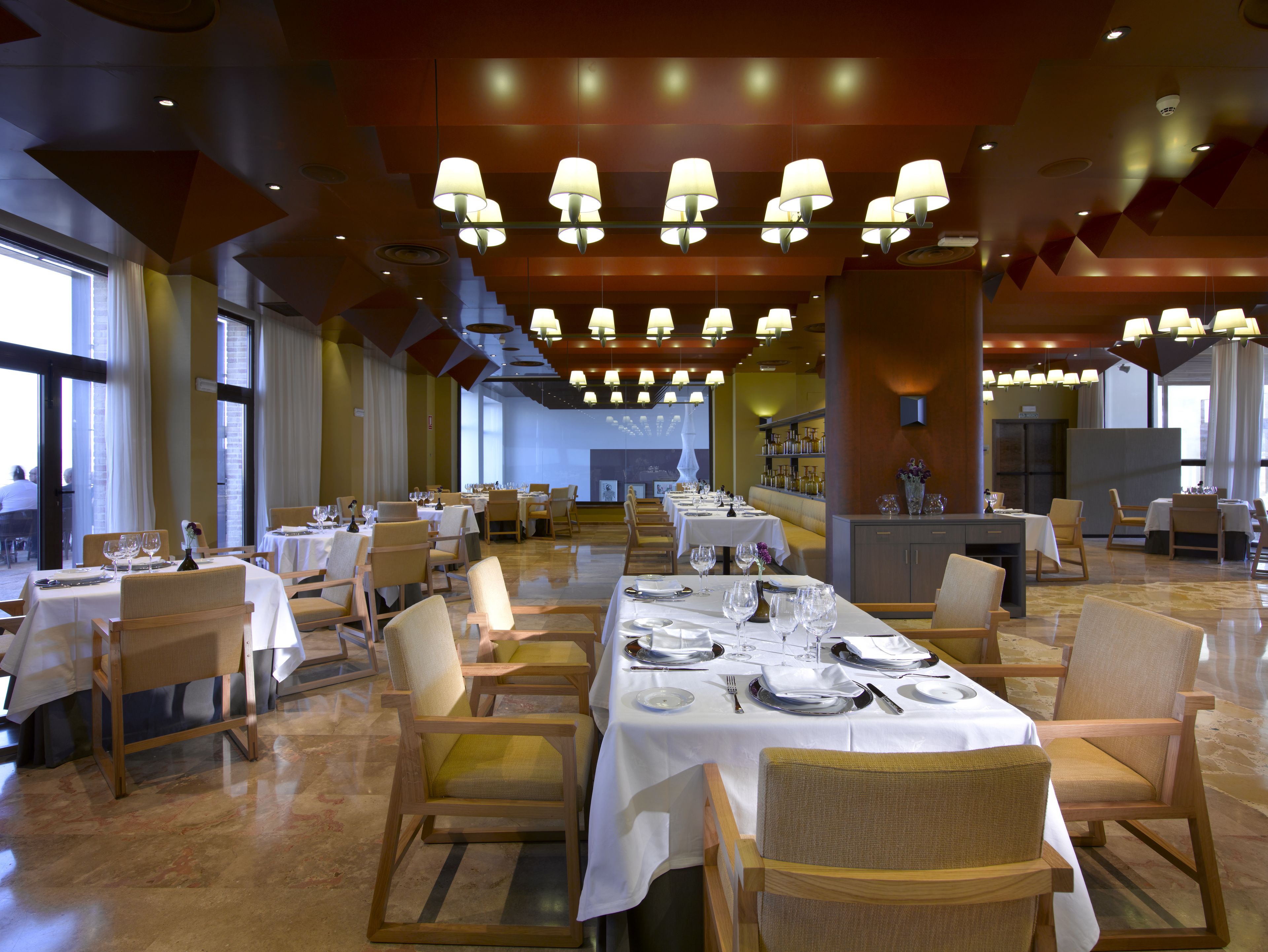 En rummelig restaurant med flere borde dækket til spisning, med et moderne interiør og masser af naturligt lys.