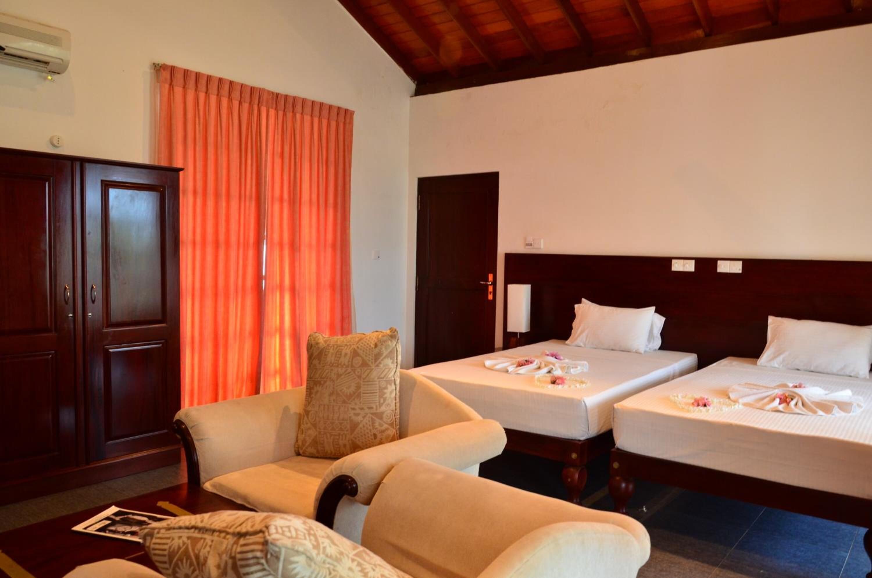 A hotel room with two single beds, a sofa, a wooden wardrobe, and a large window with curtains.