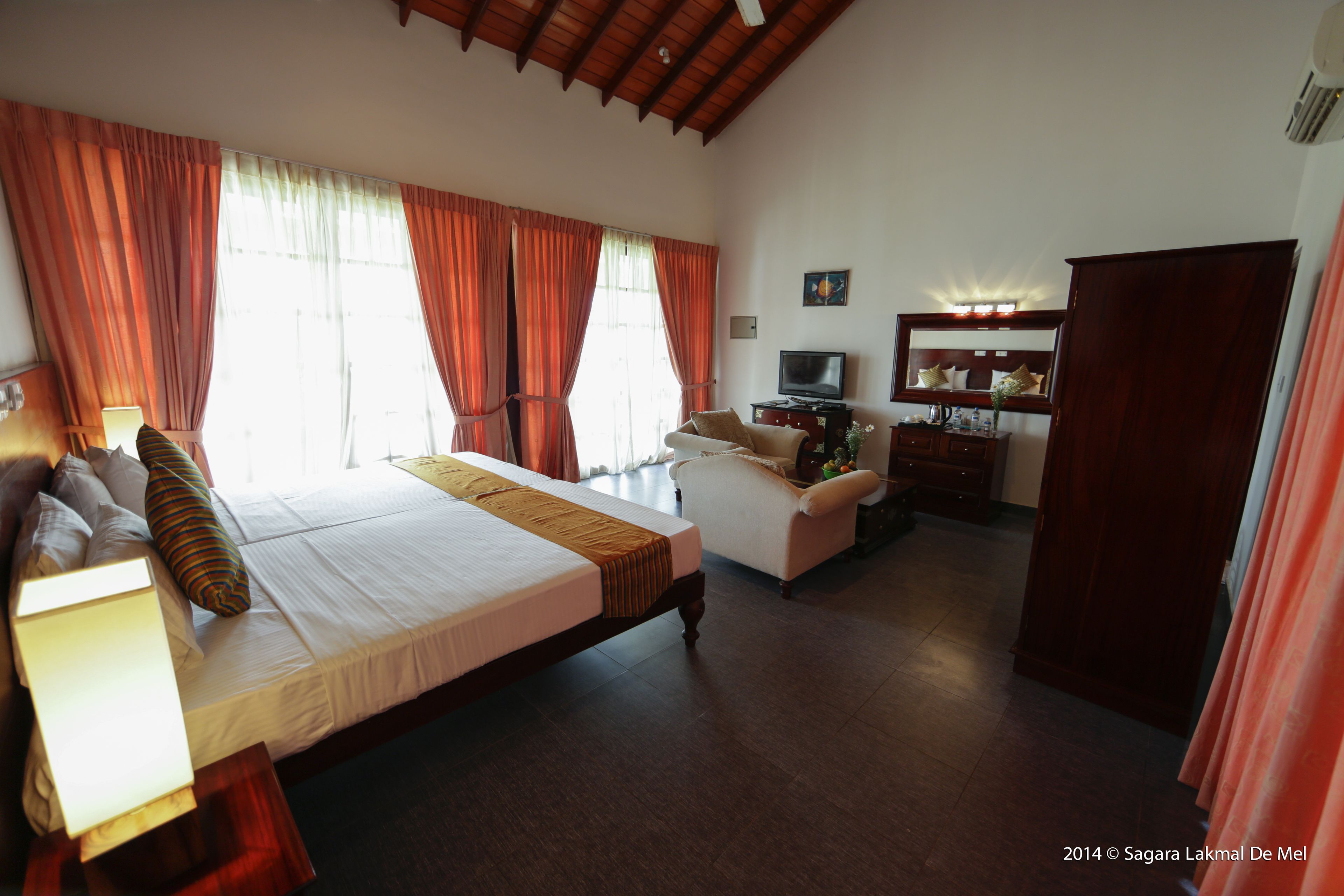 A hotel room with a large bed, a desk with a chair, a television, and a wardrobe.