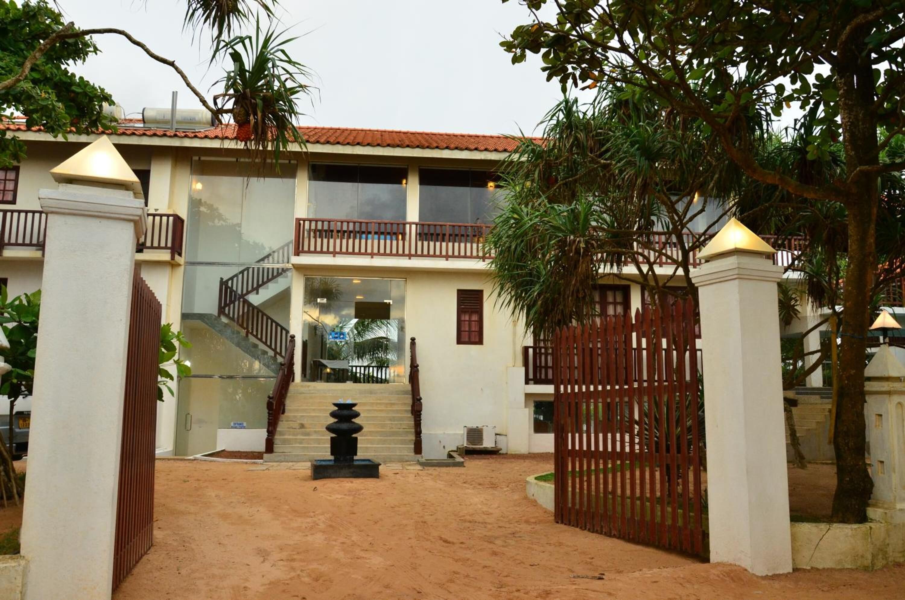 A two-story building with a staircase leading to the entrance, surrounded by a sandy courtyard and a gated entrance.