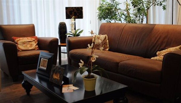 Un salón con un sofá marrón, una mesa de centro con una planta en maceta y un cuadro enmarcado.