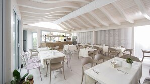A spacious dining area with white tables and chairs, a high ceiling with wooden beams, and a view of the kitchen in the background. - Hotel Torino (Parma)