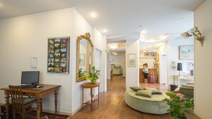 A spacious living area with a wooden desk, a round sofa, and a dining table. There is a large mirror on the wall and a potted plant on the floor. - Hotel Torino (Parma)
