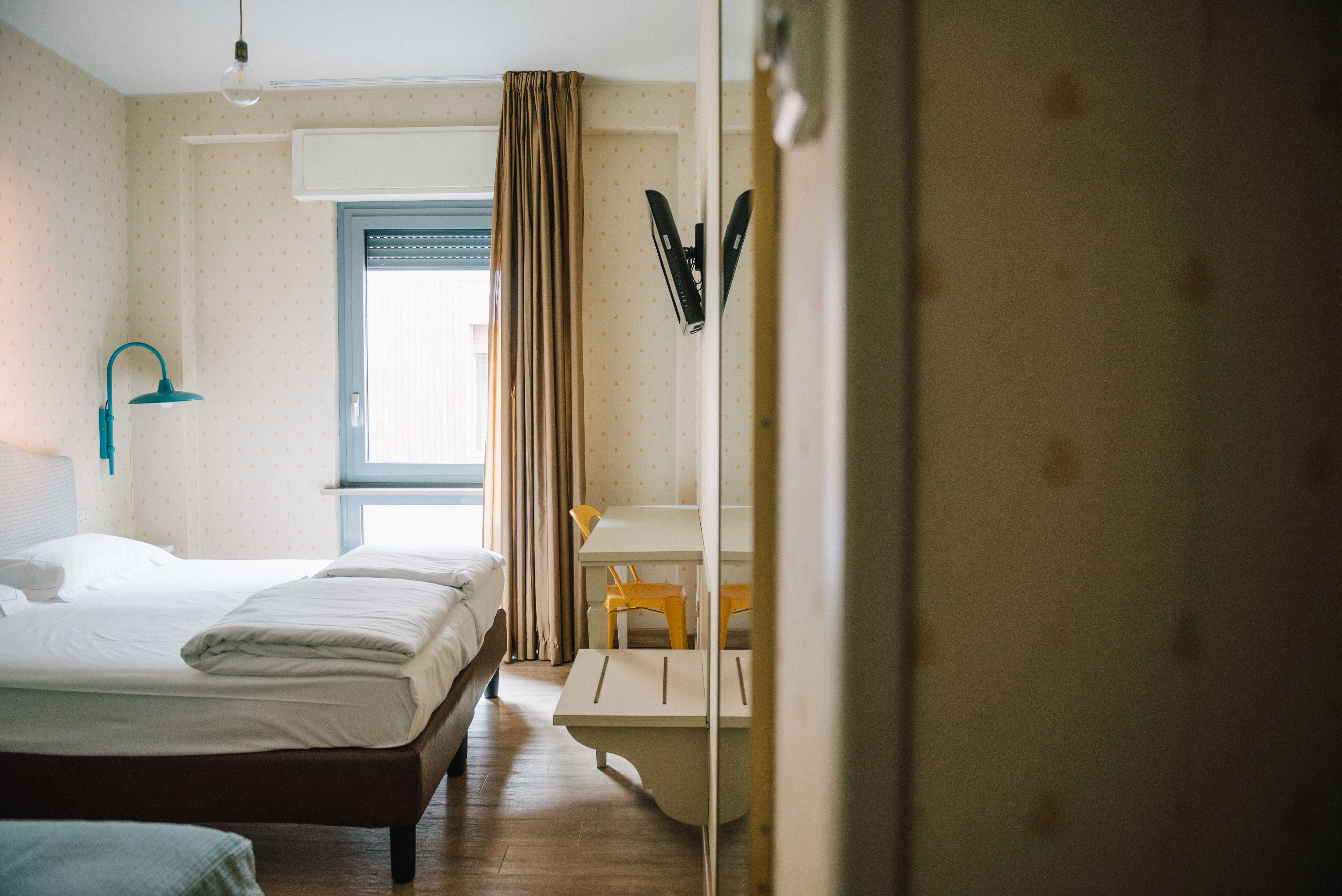 A hotel room with a bed, a desk, a chair, and a window with curtains.