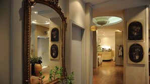 A hallway with a large mirror, framed artwork, and a chandelier. - Hotel Torino (Parma)