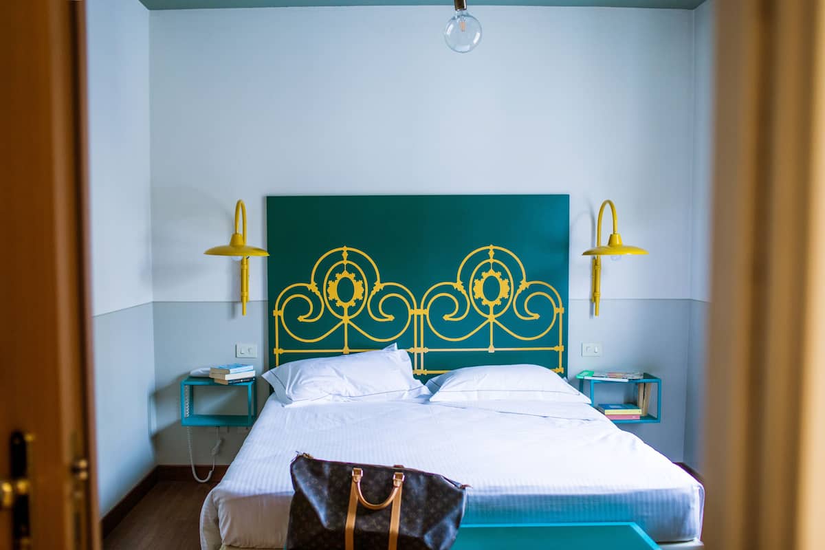A neatly made bed with white linens, a teal headboard, and two bedside tables with lamps.