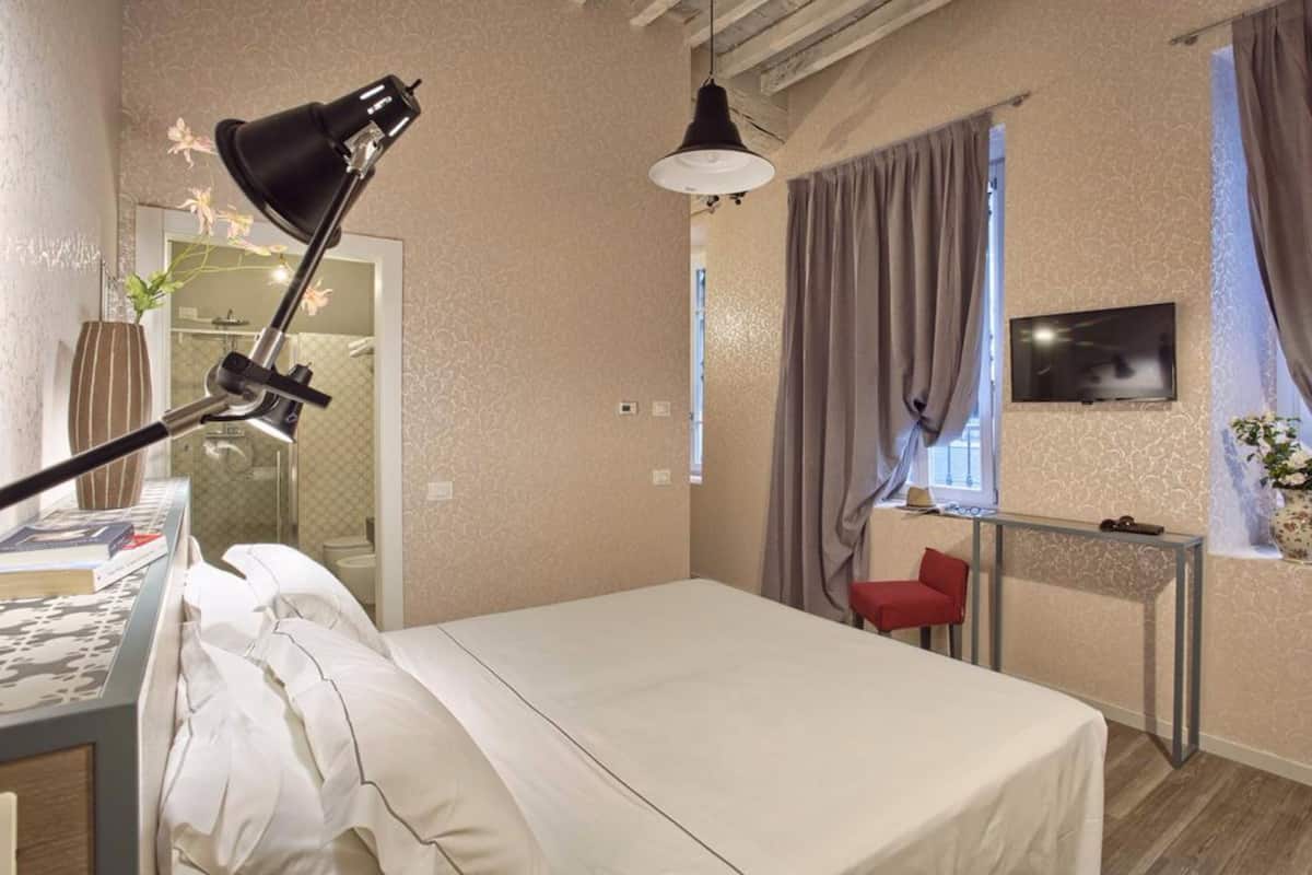 A bedroom with a bed, a desk, a chair, a TV, and a window with curtains.