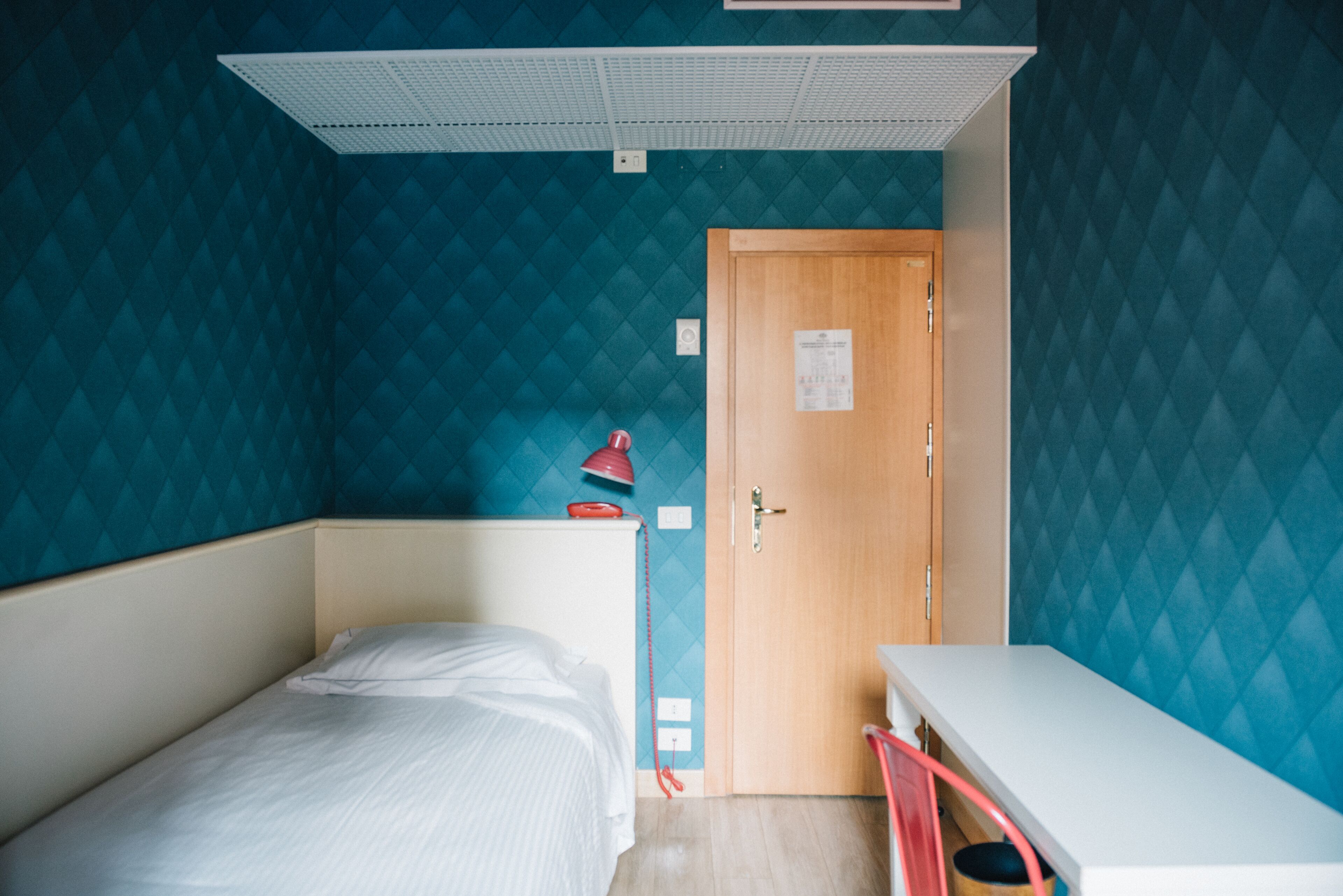 Quarto pequeno com uma cama, uma escrivaninha e uma porta.