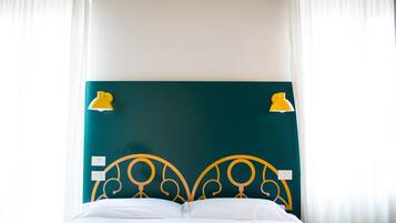 Ein Bett mit weißer Bettwäsche, einem türkisblauen Kopfteil und zwei an der Wand befestigten gelben Lampen.