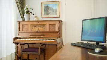 Een piano, een computer en een stoel in een kamer met een deur en een raam.