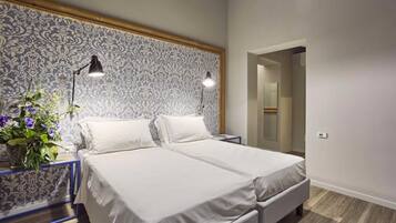 Une chambre avec deux lits, une table de chevet avec une lampe et un mur recouvert d’un papier peint à motifs.