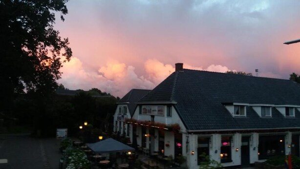 A building with a dark roof and white walls, featuring a porch with outdoor seating and string lights. - De Koningsherberg (Anloo)