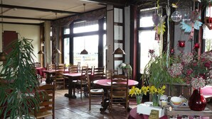 A restaurant with wooden tables and chairs, potted plants, and hanging decorations. - De Koningsherberg (Anloo)