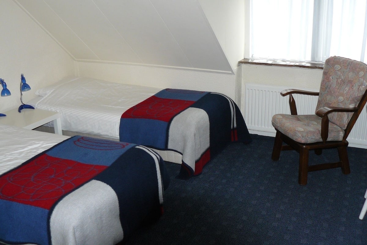 Ein Hotelzimmer mit zwei Einzelbetten, einem Holzbett, einem Tisch und einem Fenster mit Jalousien.