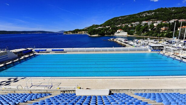 A swimming pool with blue water, surrounded by blue chairs and a dock with boats. - Jadran-Zvončac Accommodations - Hostel (Split)