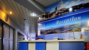 A reception area with a cityscape mural, a clock, and a reception desk. - Jadran-Zvončac Accommodations - Hostel (Split)