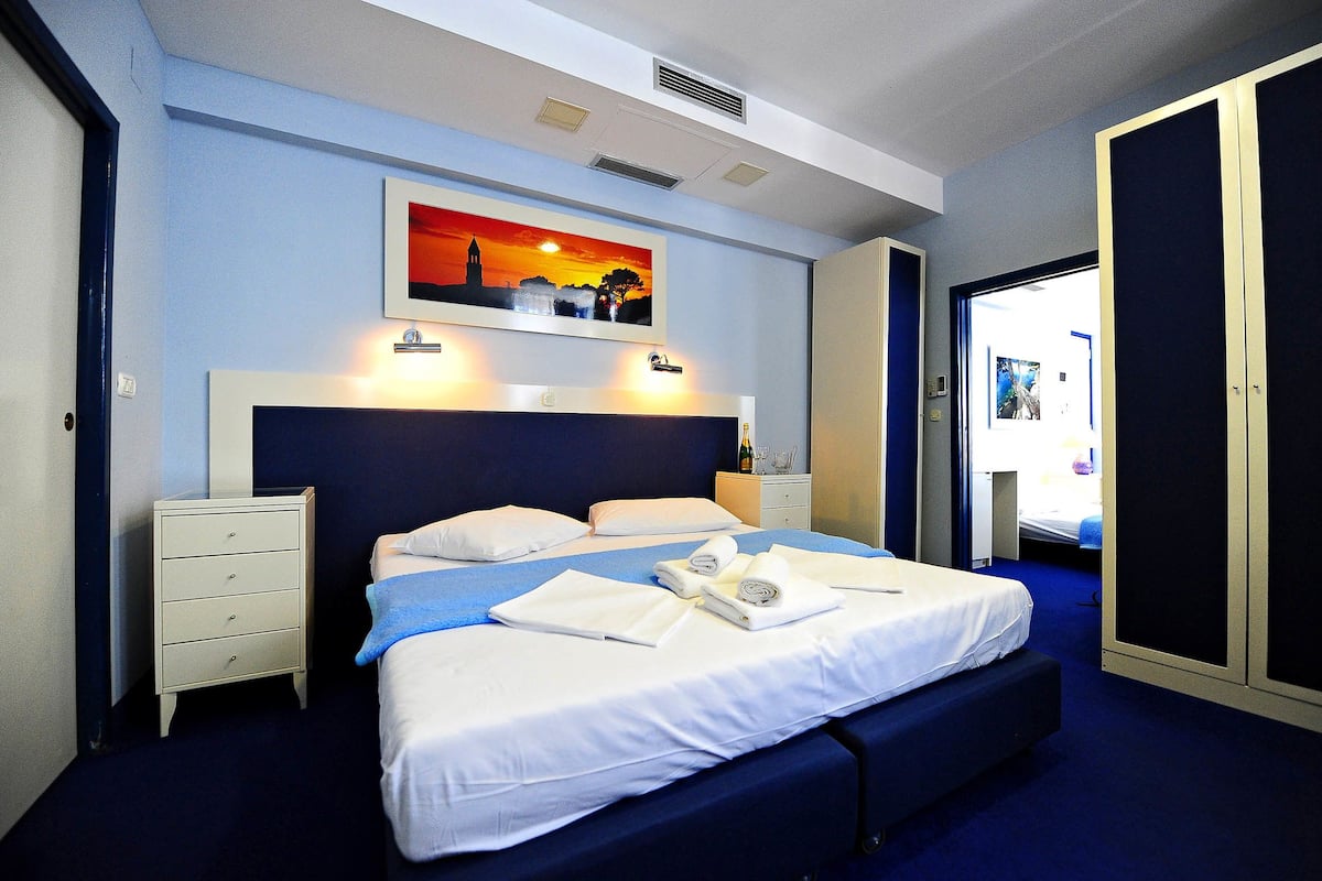 A hotel room with a bed, a nightstand, a painting, and a door.