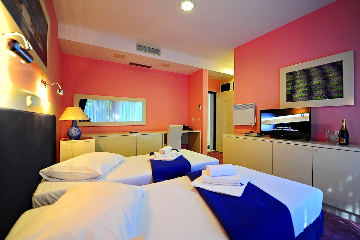 A hotel room with two beds, a television, a desk, and a window with curtains.
