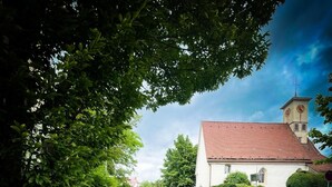 A church with a clock tower, surrounded by greenery and a cobblestone path.