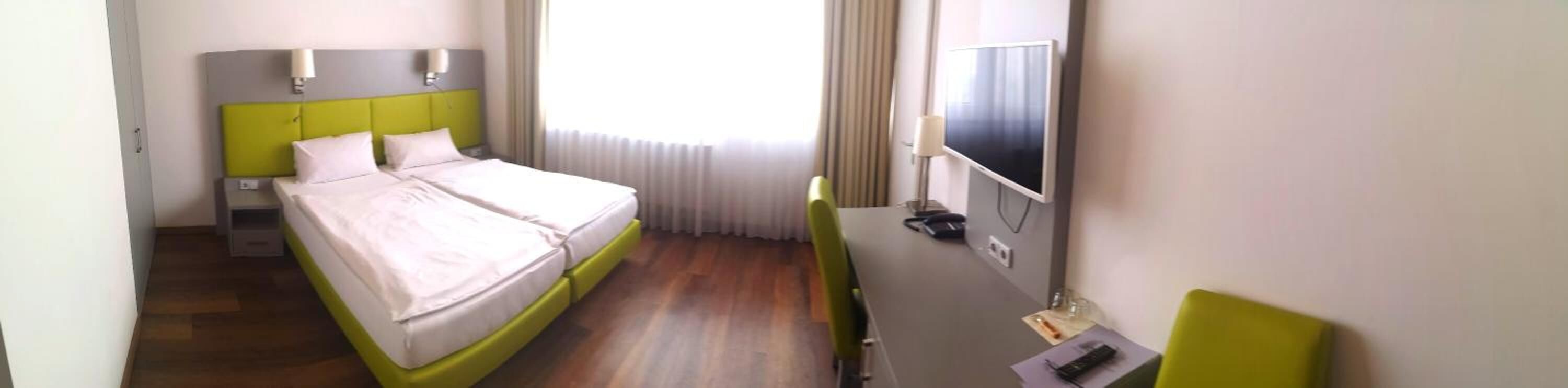 Une chambre d’hôtel avec un lit, un bureau, une télévision et une fenêtre avec des rideaux.