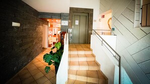 A staircase with beige tiles leading to a door, a stone wall on the left, and a white wall with a mirror on the right.