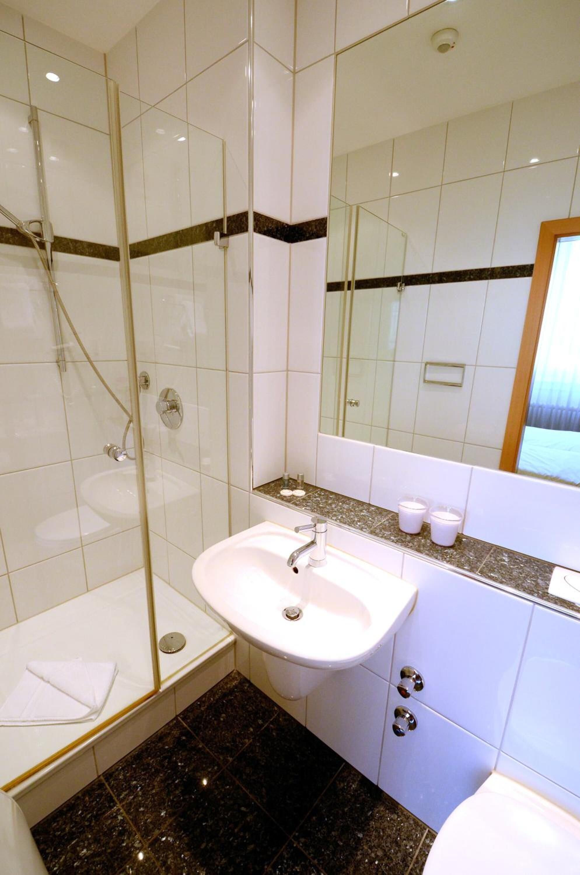 A modern bathroom with a glass-enclosed shower, a white sink, and a large mirror.