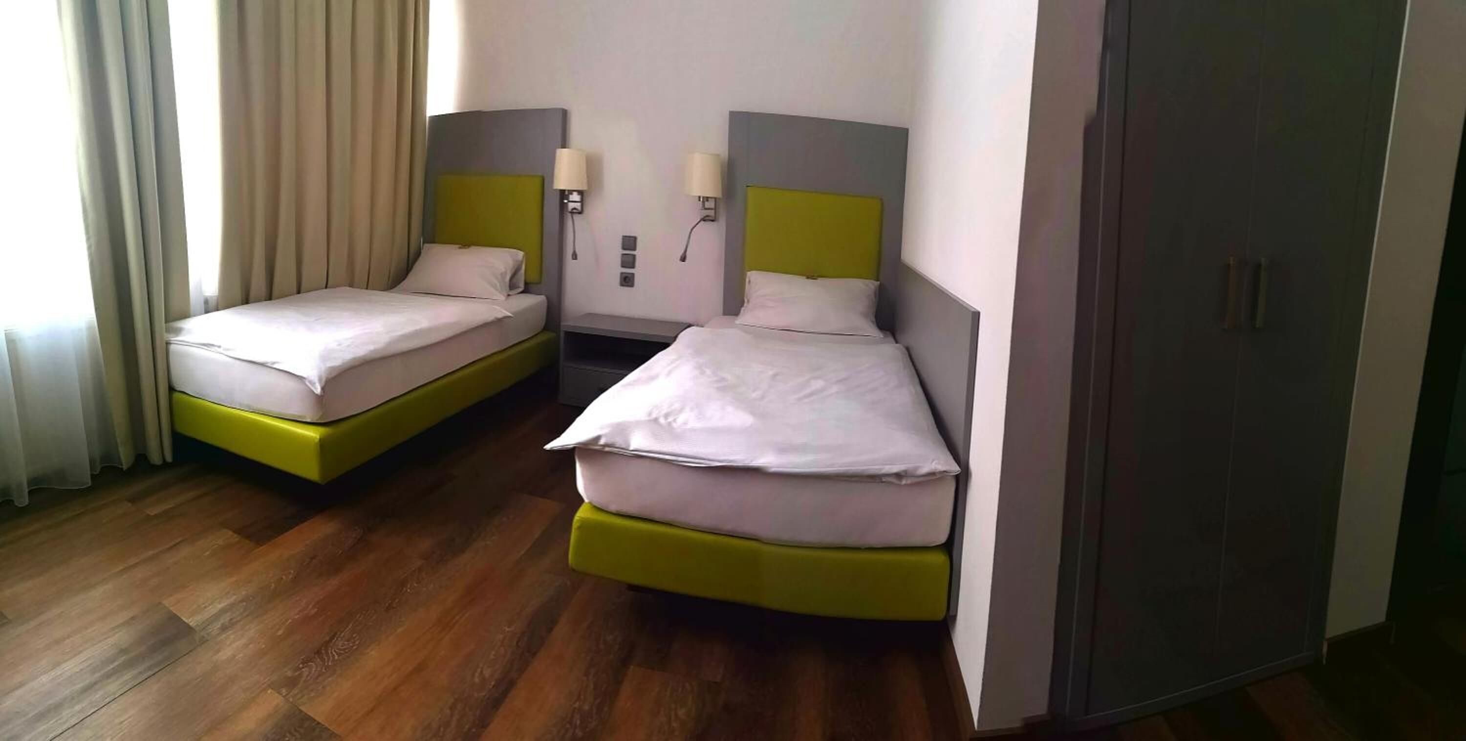 A hotel room with two single beds, a wardrobe, and a nightstand with lamps.