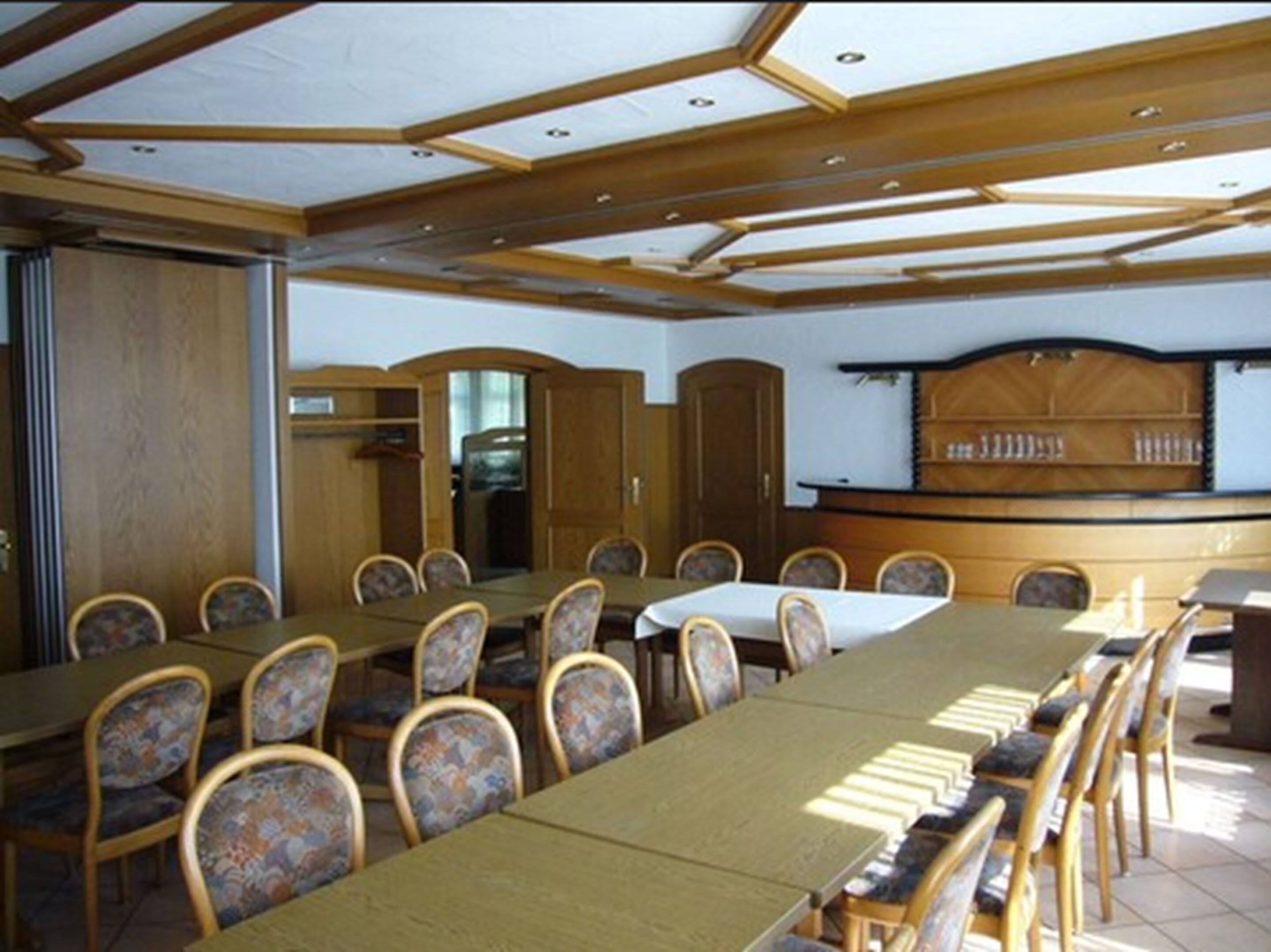 A conference room with a long table and chairs, wooden paneling, and a counter with a display.