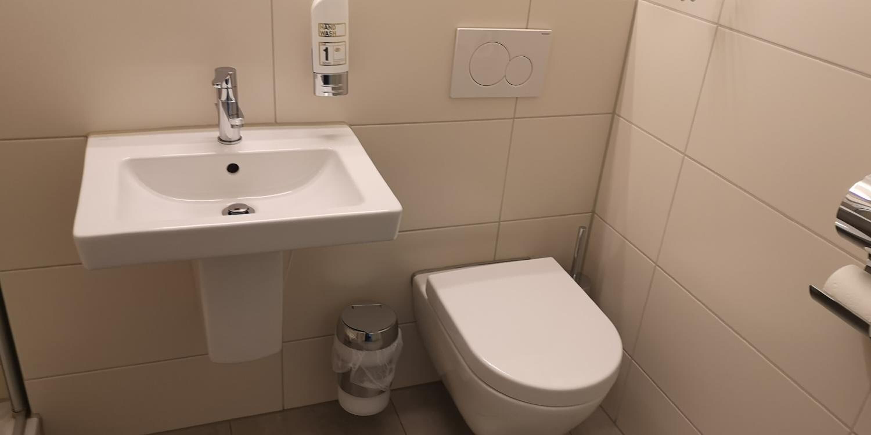A bathroom with a white sink, a toilet, and a trash bin.