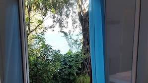 Une chambre avec un lit, une porte-fenêtre coulissante donnant sur un balcon agrémenté de plantes et offrant une vue sur le ciel.