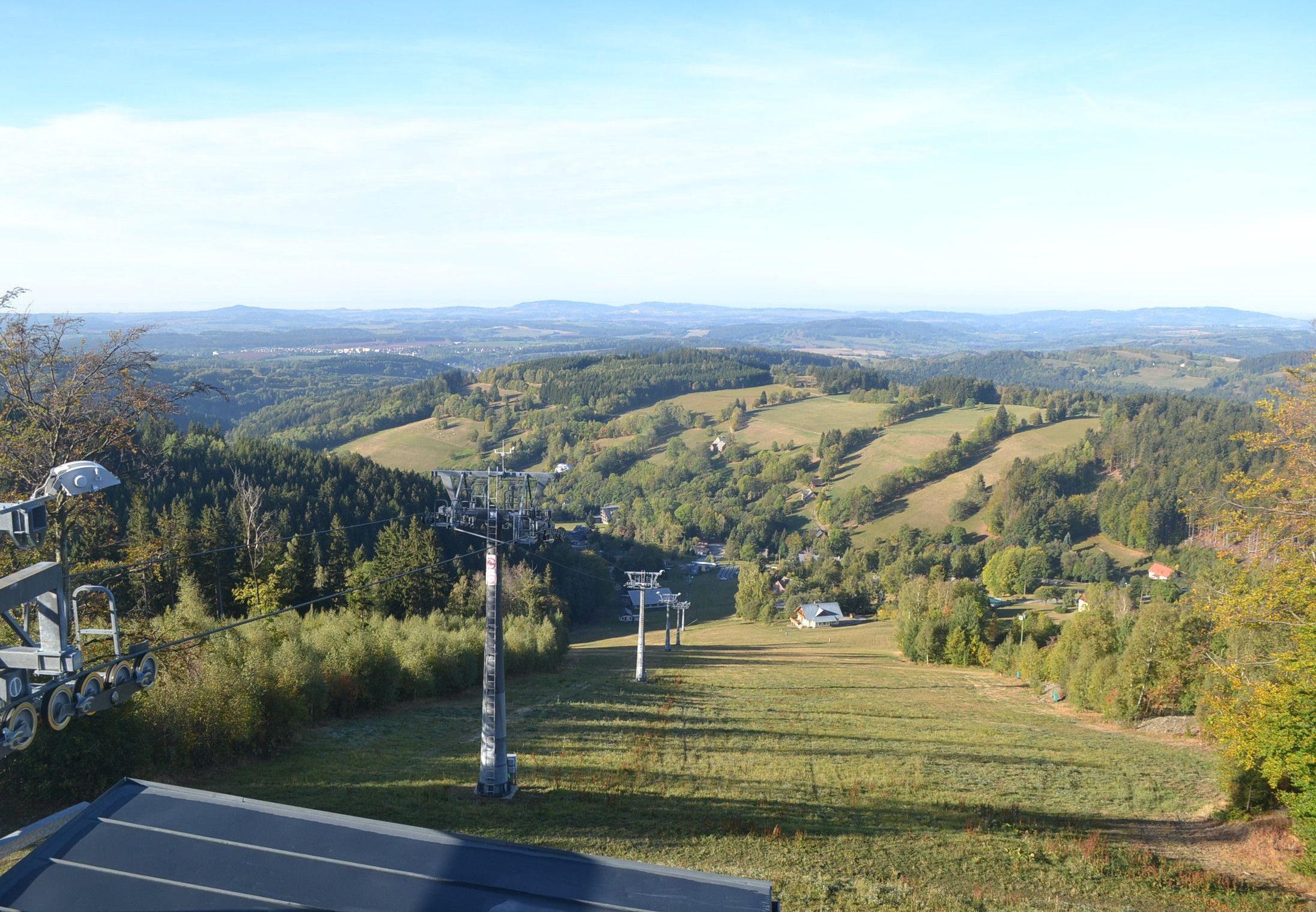 Une vue panoramique d’un paysage montagneux, avec un télésiège et un petit bâtiment situé dans la vallée.