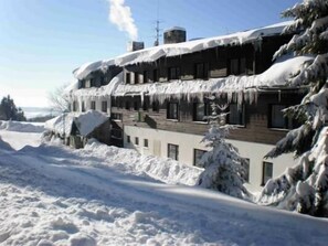 Un immeuble à plusieurs étages, dont les toits sont recouverts de neige, se dressant au milieu d’un paysage enneigé.
