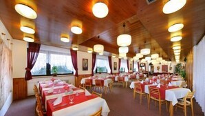A restaurant with multiple tables set for dining, wooden ceiling, and large windows with curtains. - Hotel Diana (Benecko)
