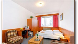 A hotel room with a bed, two sofas, a small table, a desk with a computer, a radiator, and a window with curtains. - Hotel Diana (Benecko)