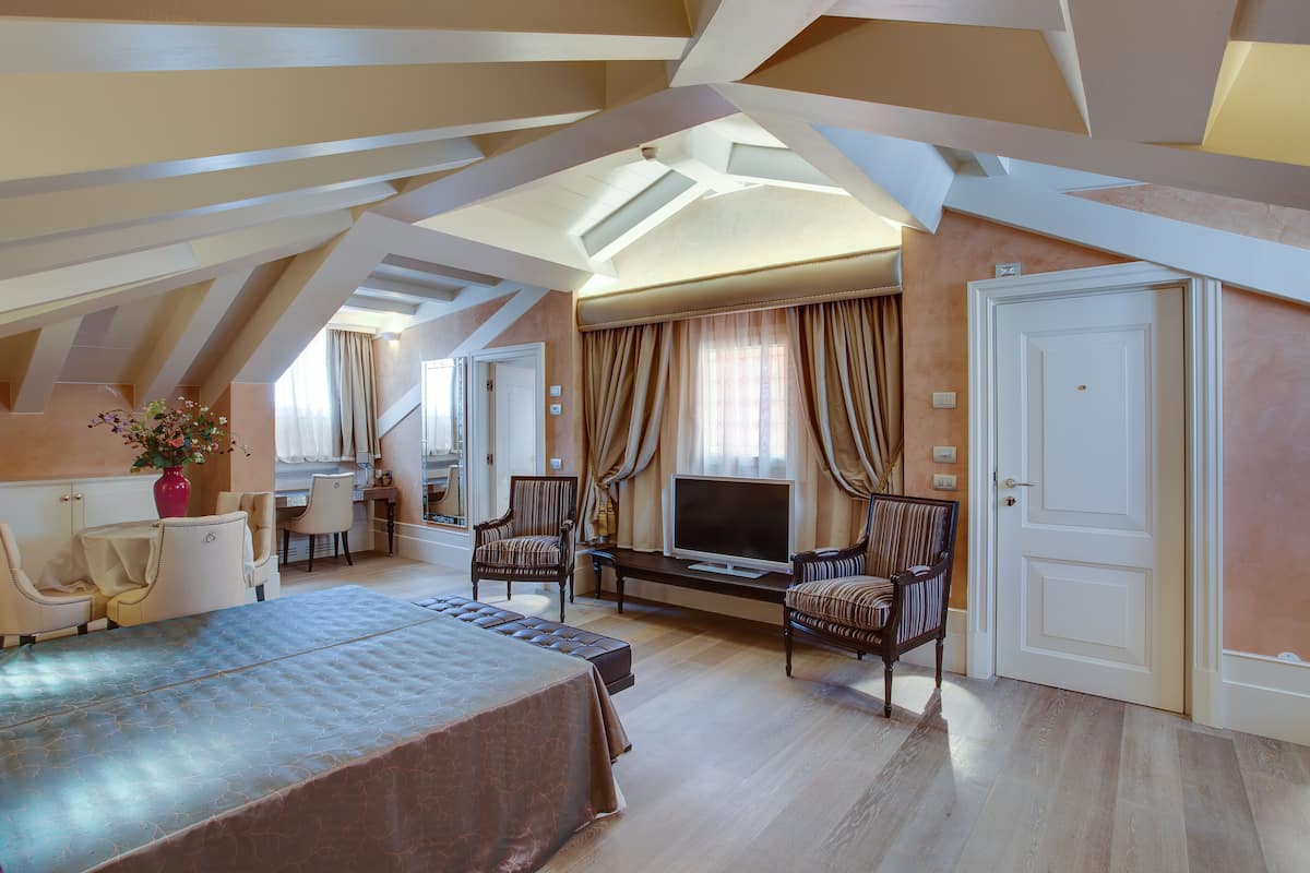 Une chambre spacieuse avec un grand lit, une télévision et deux fauteuils.