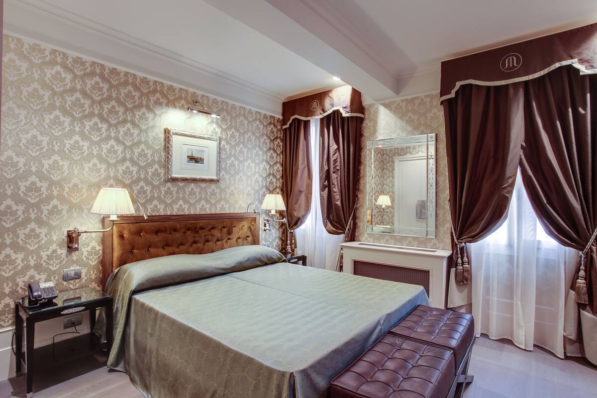 Une chambre d’hôtel avec un grand lit, une table de chevet avec une lampe, un miroir et un banc.