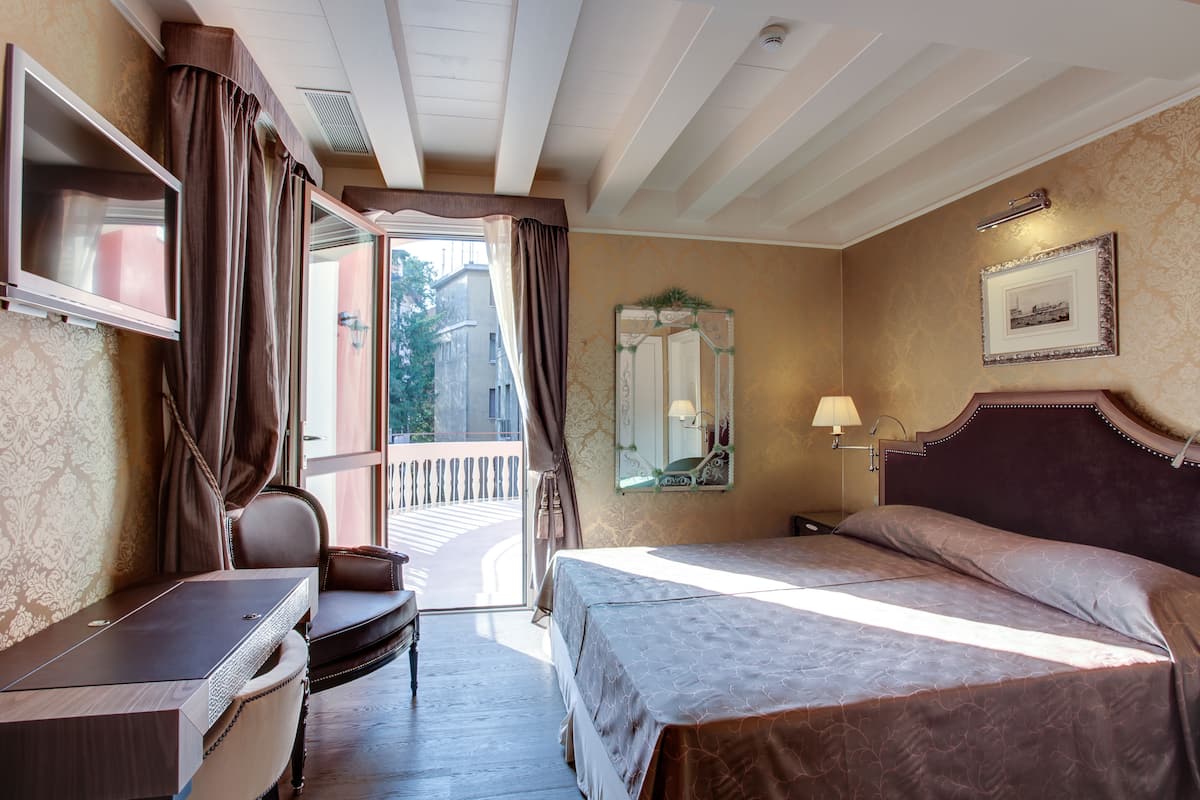 Une chambre d’hôtel avec un lit, un bureau, une chaise, un miroir et une fenêtre avec des rideaux.