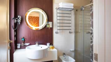 A bathroom with a round mirror, two sinks, a bidet, a towel rack, and a shower area.