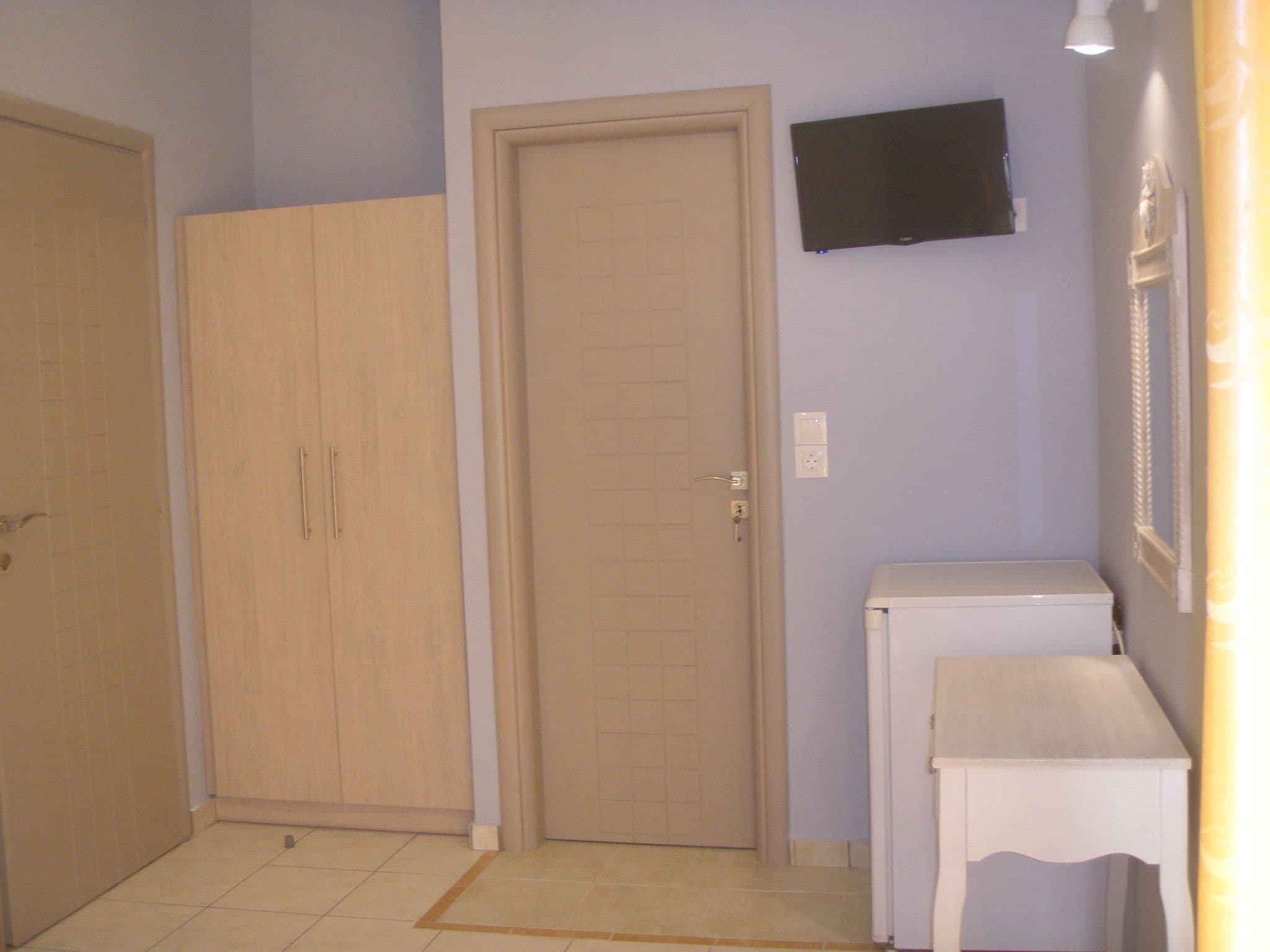 A small, enclosed room with a door, a television mounted on the wall, and a small table.