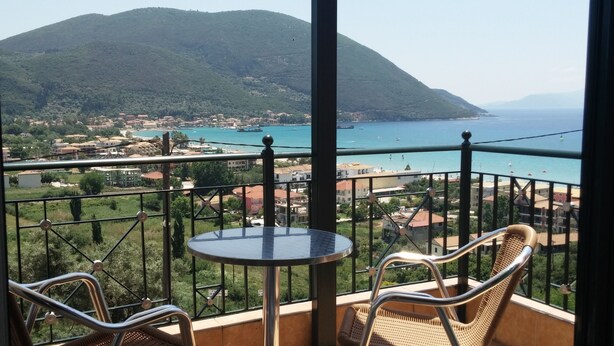 Un balcon agrémenté de fauteuils en osier et d’une petite table, d’où l’on peut admirer une ville côtière et une montagne.