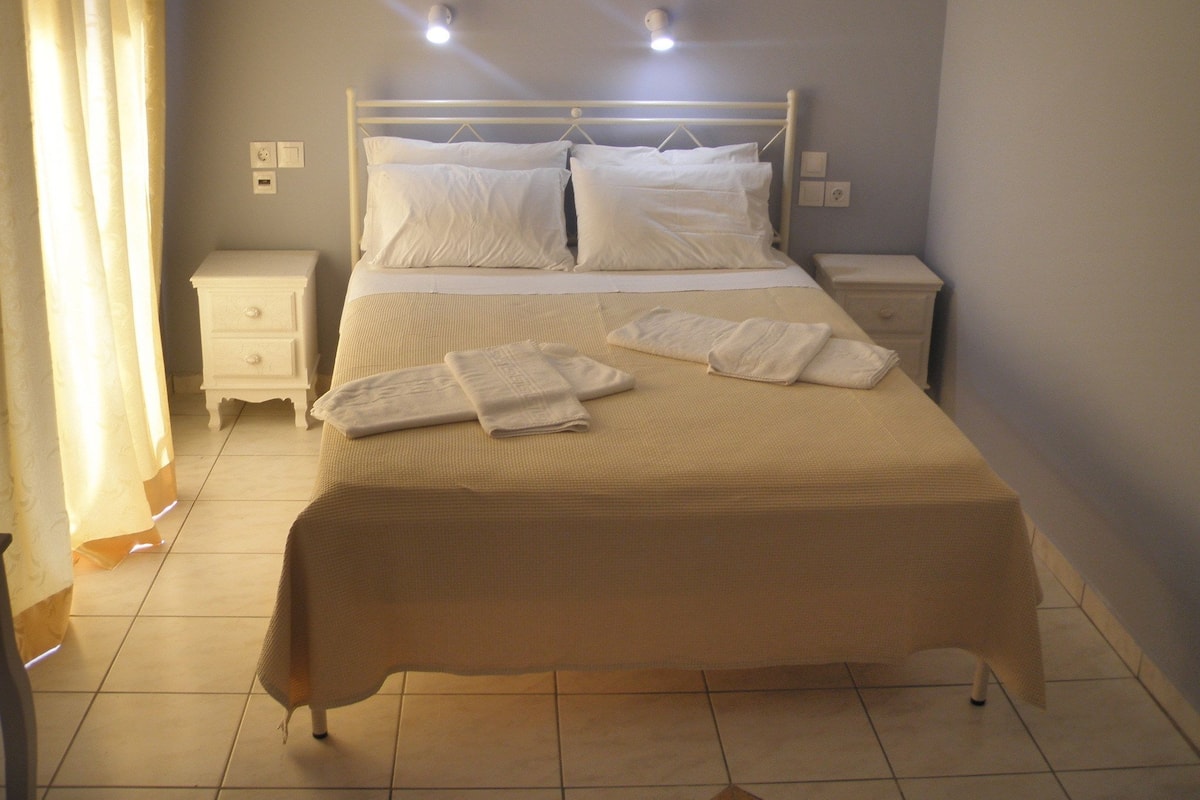 Una cama bien hecha con sábanas y toallas blancas, una mesita de noche y una mesilla.