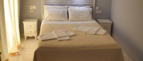 Un lit bien fait, avec du linge de lit et des serviettes blanches, une table de chevet et une petite table à côté du lit.