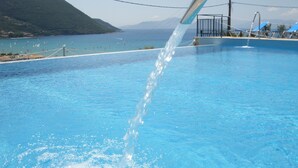 Une piscine à l’eau cristalline, une fontaine et une vue sur la mer et les collines en arrière-plan.