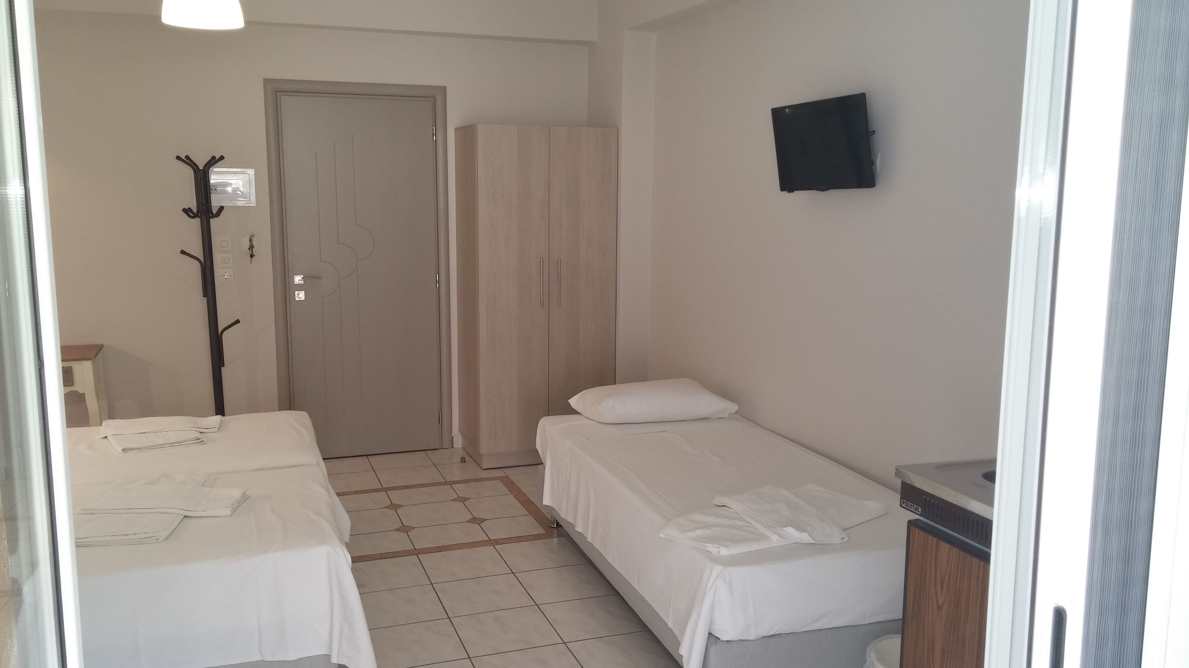Een hotelkamer met twee bedden, een kledingkast, een kapstok en een televisie aan de muur.