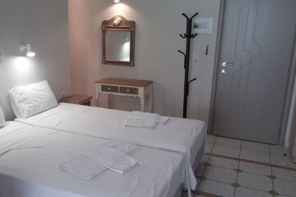 Una habitación de hotel con dos camas, una mesita de noche de madera, un espejo, un perchero y una puerta con manija.